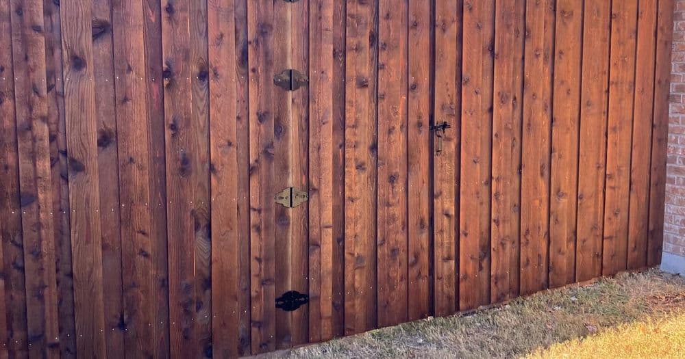 Wooden fence gate with decorative hinges and a lock, set against a brick wall.