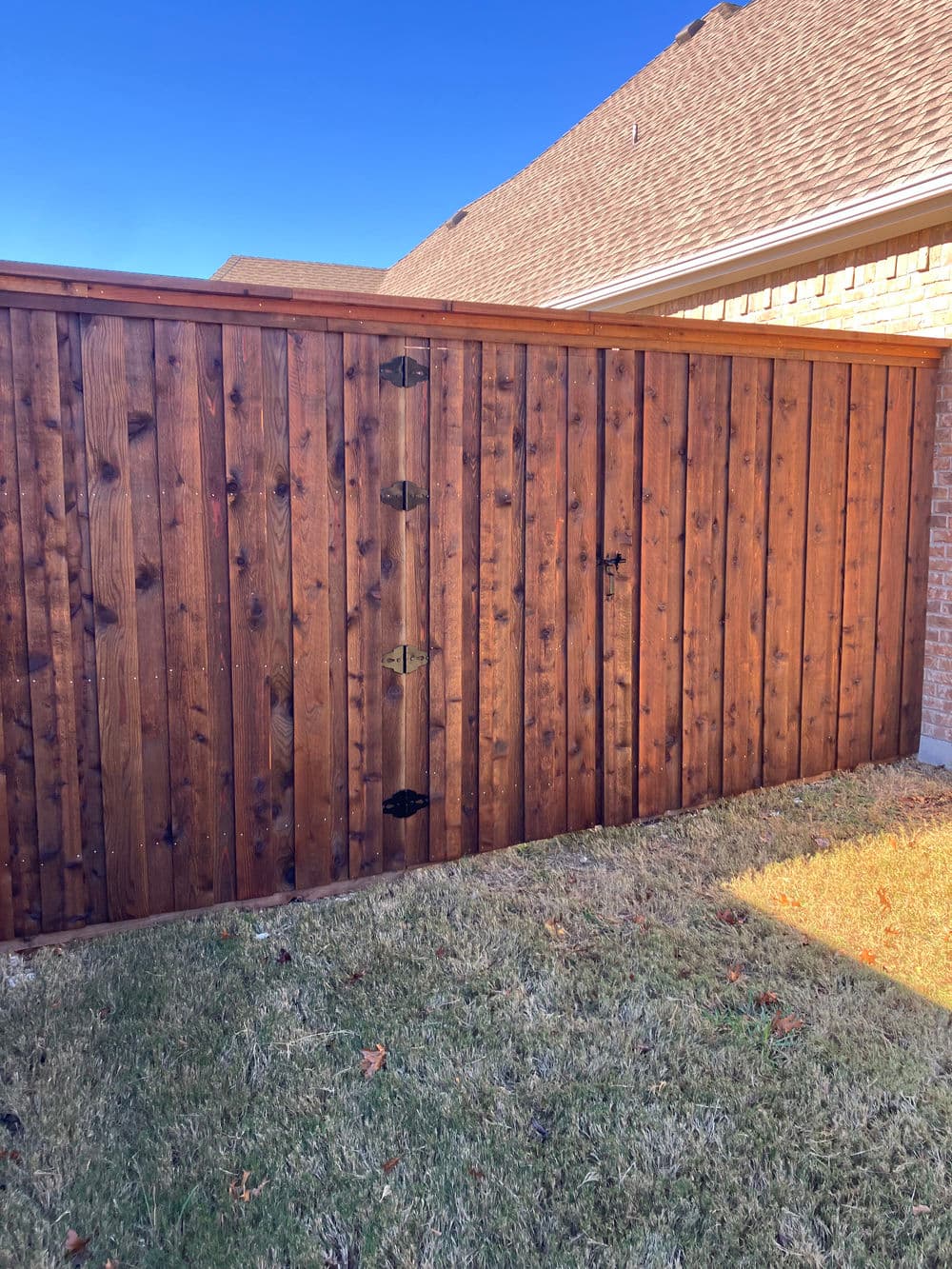 Wooden fence gate next to a brick house with clear blue sky above.